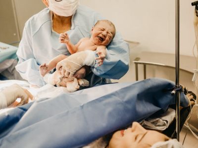 A doctor holds a newborn baby in a hospital setting post-delivery.