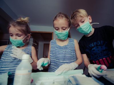 Children pretending to be doctors in a playful indoor setting, wearing masks and gloves.